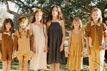 Children in matching outfits standing outdoors with trees in the background