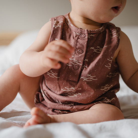 Baby in a patterned romper sitting on a bed