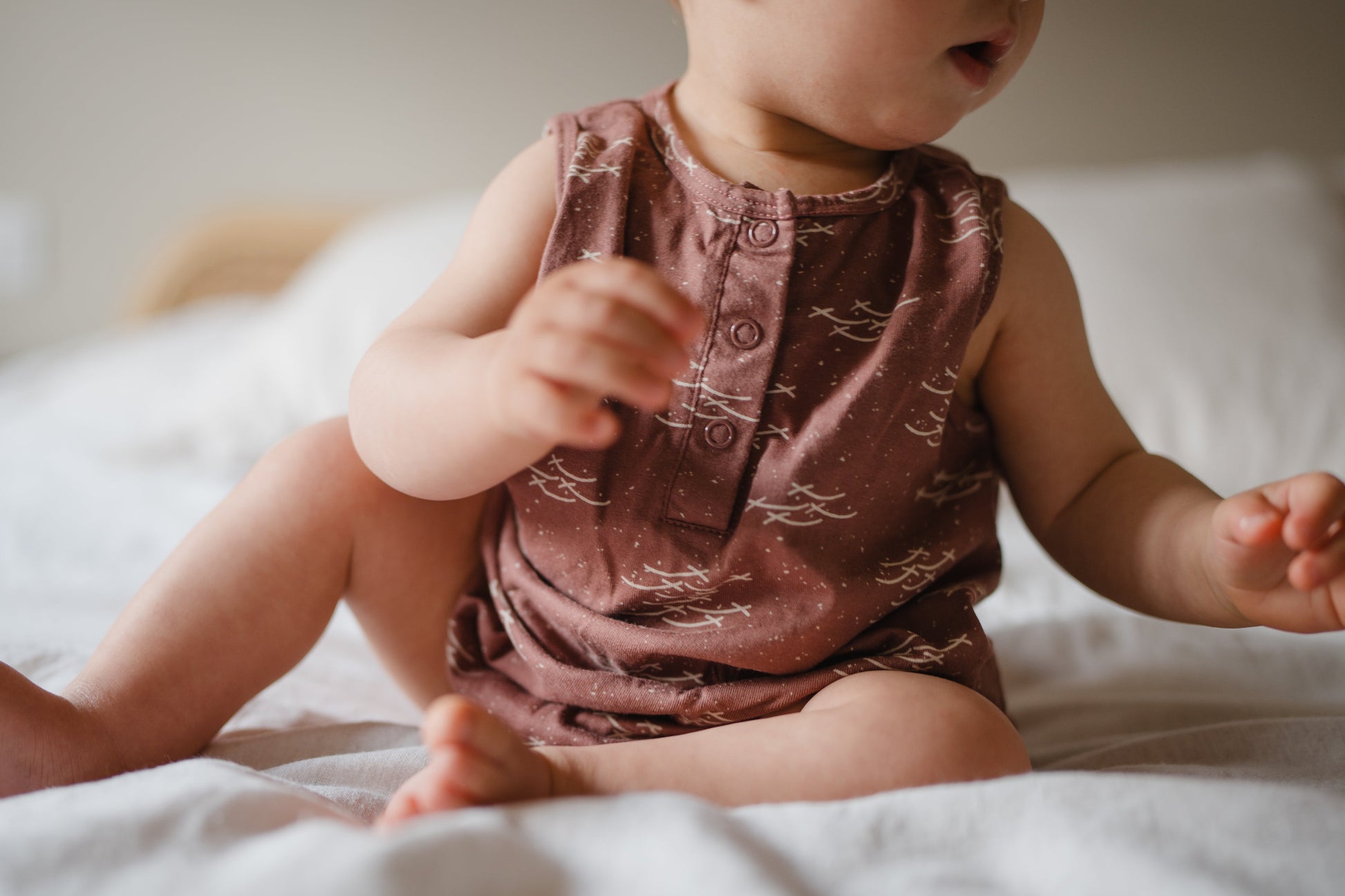 Baby in a patterned romper sitting on a bed