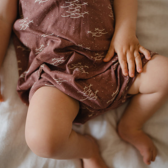 Baby wearing a patterned romper sitting on a bed