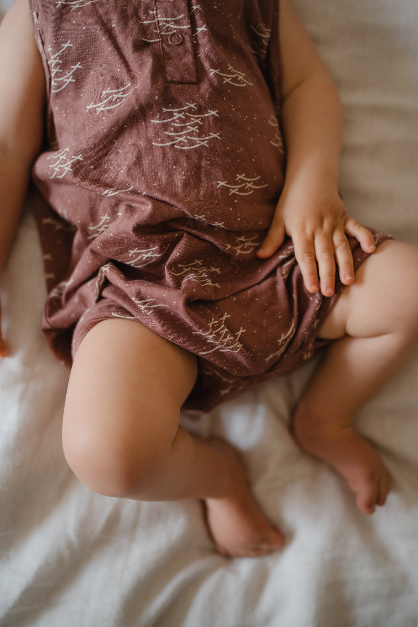 Baby wearing a patterned romper sitting on a bed