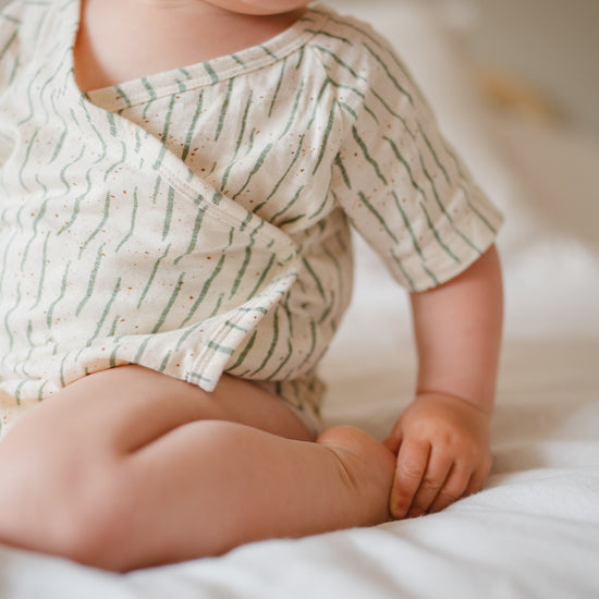 Baby wearing a patterned onesie sitting on a soft surface