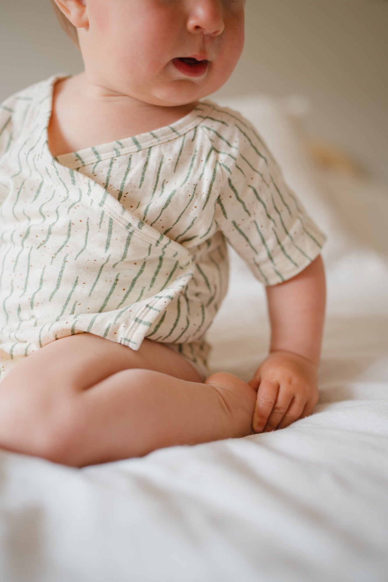 Baby wearing a patterned onesie sitting on a soft surface